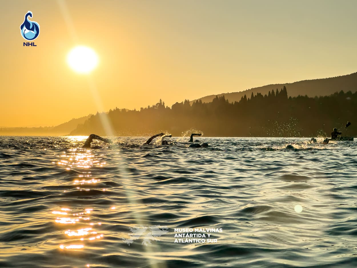Nadadores cruzando el lago Nahuel Huapi al atardecer, con la cordillera de fondo