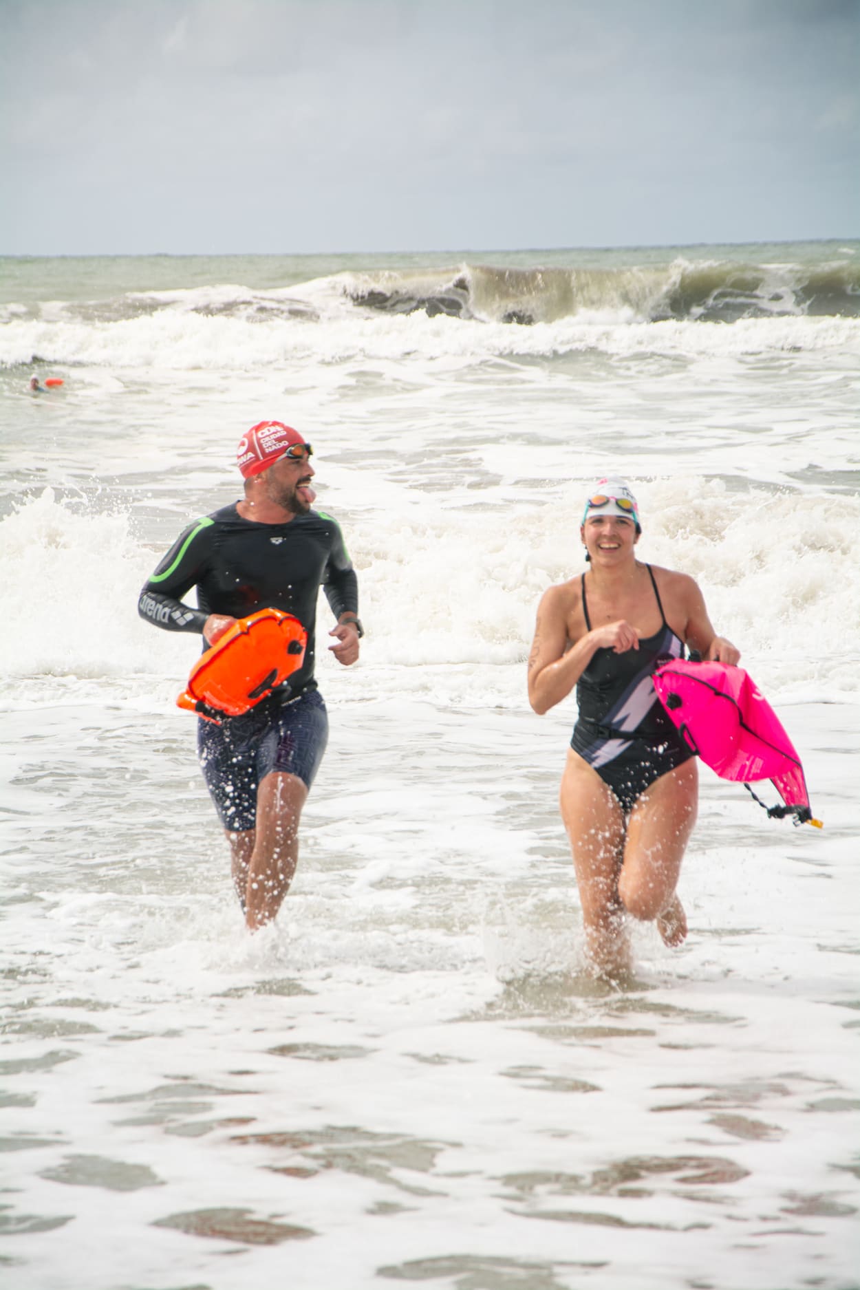 Dos nadadores saliendo del mar entre olas, sonriendo