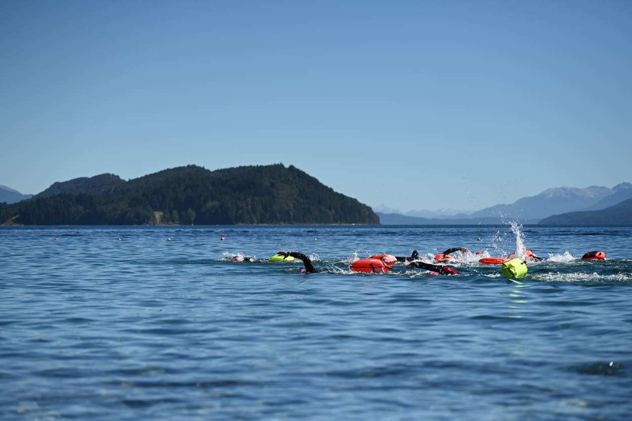Nadadores cruzando el lago Nahuel Huapi con la isla Huemul de fondo